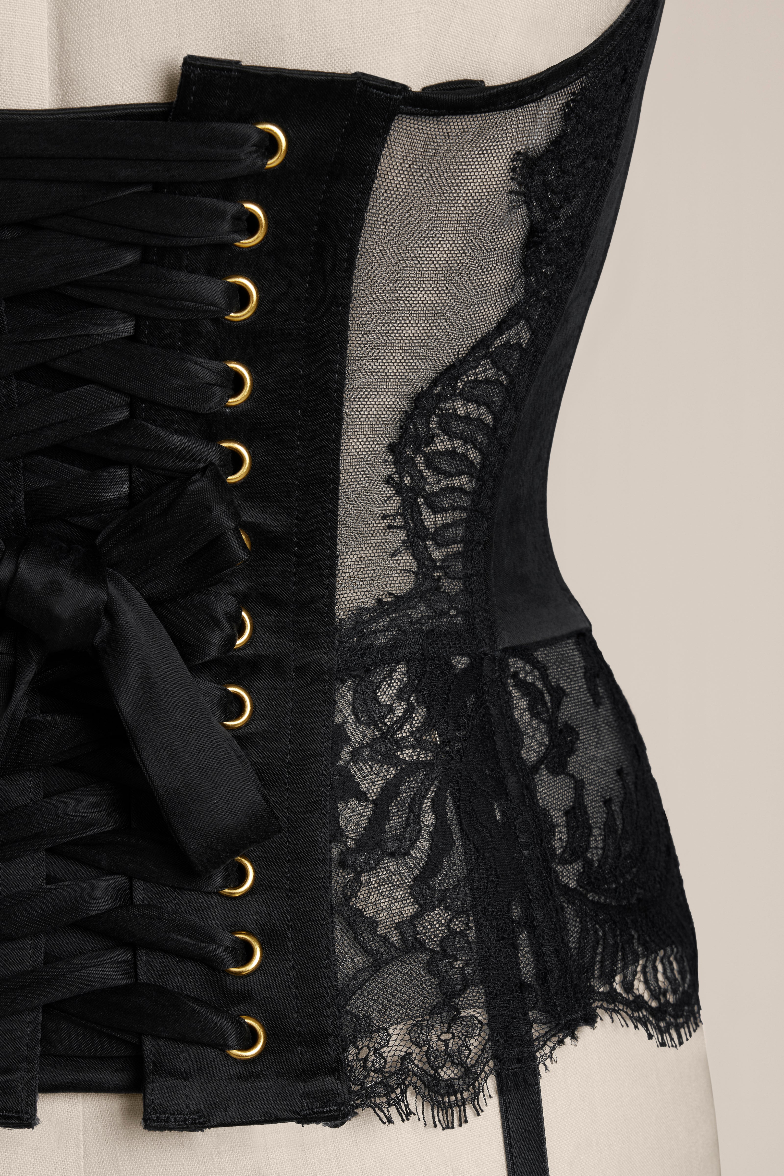 Black corset with lace details and gold hooks on a neutral background