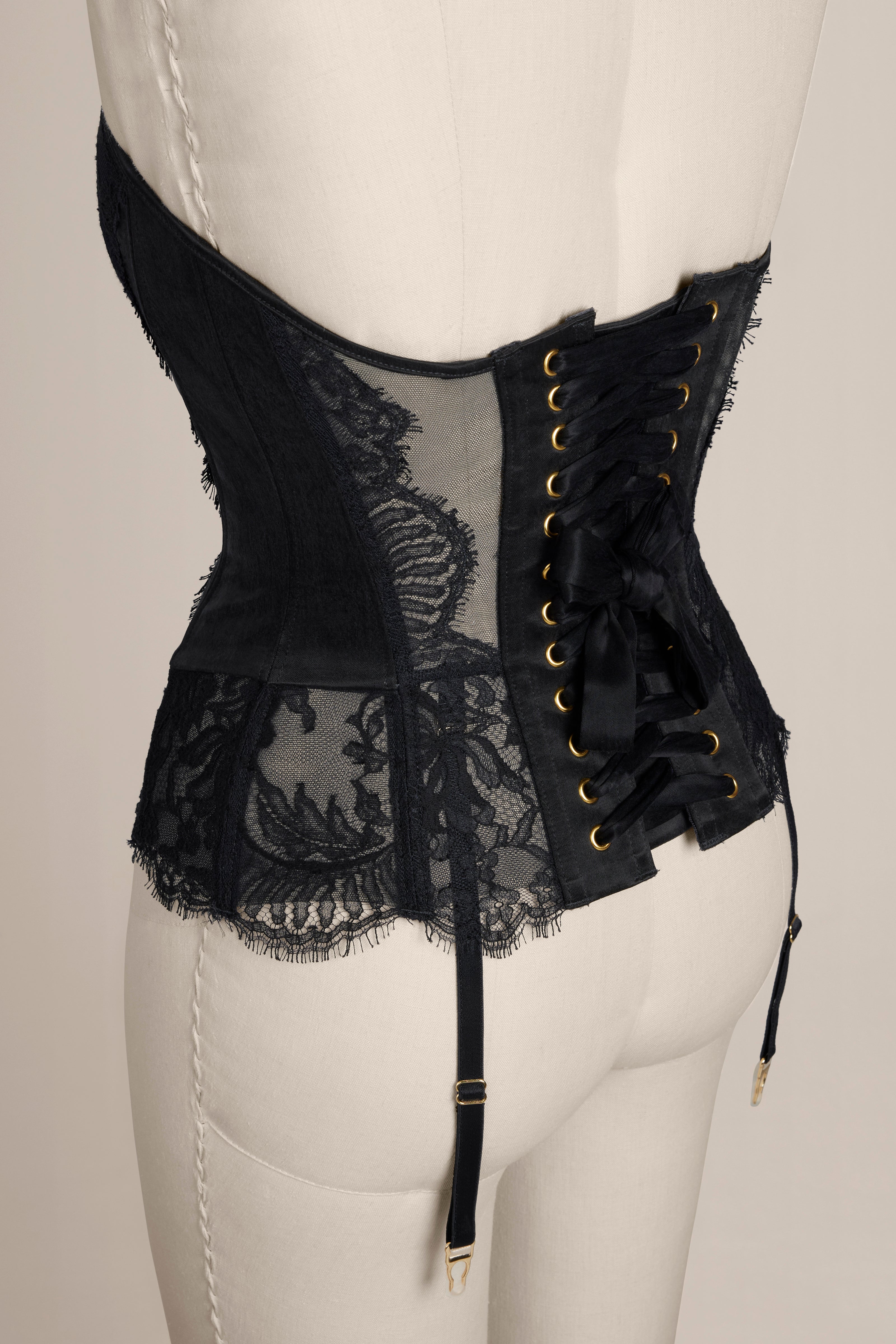 Black corset with lace details on a mannequin against a neutral background