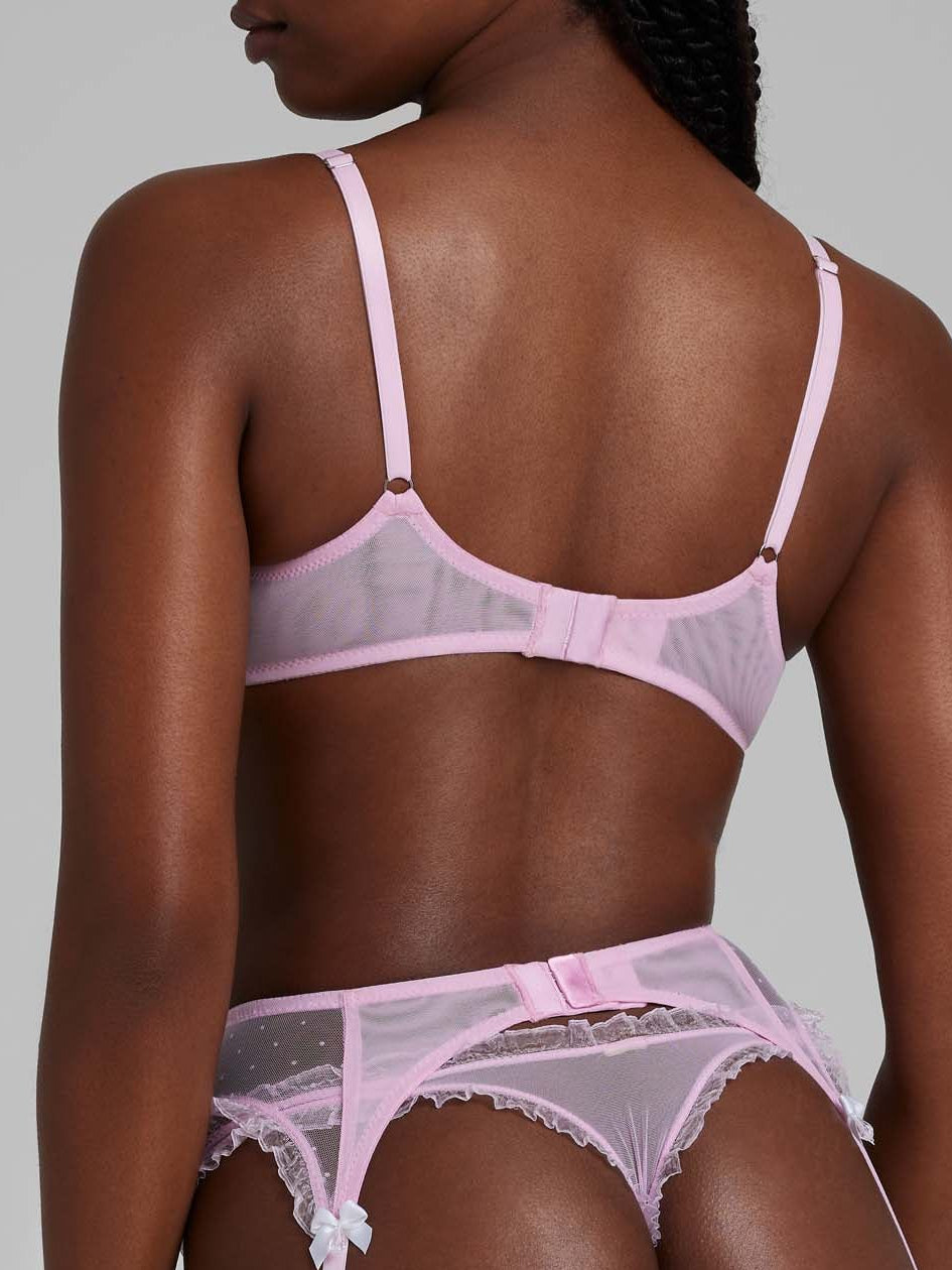 Woman wearing bubble-gum pink lace lingerie set with bra, thong and suspenders from behind