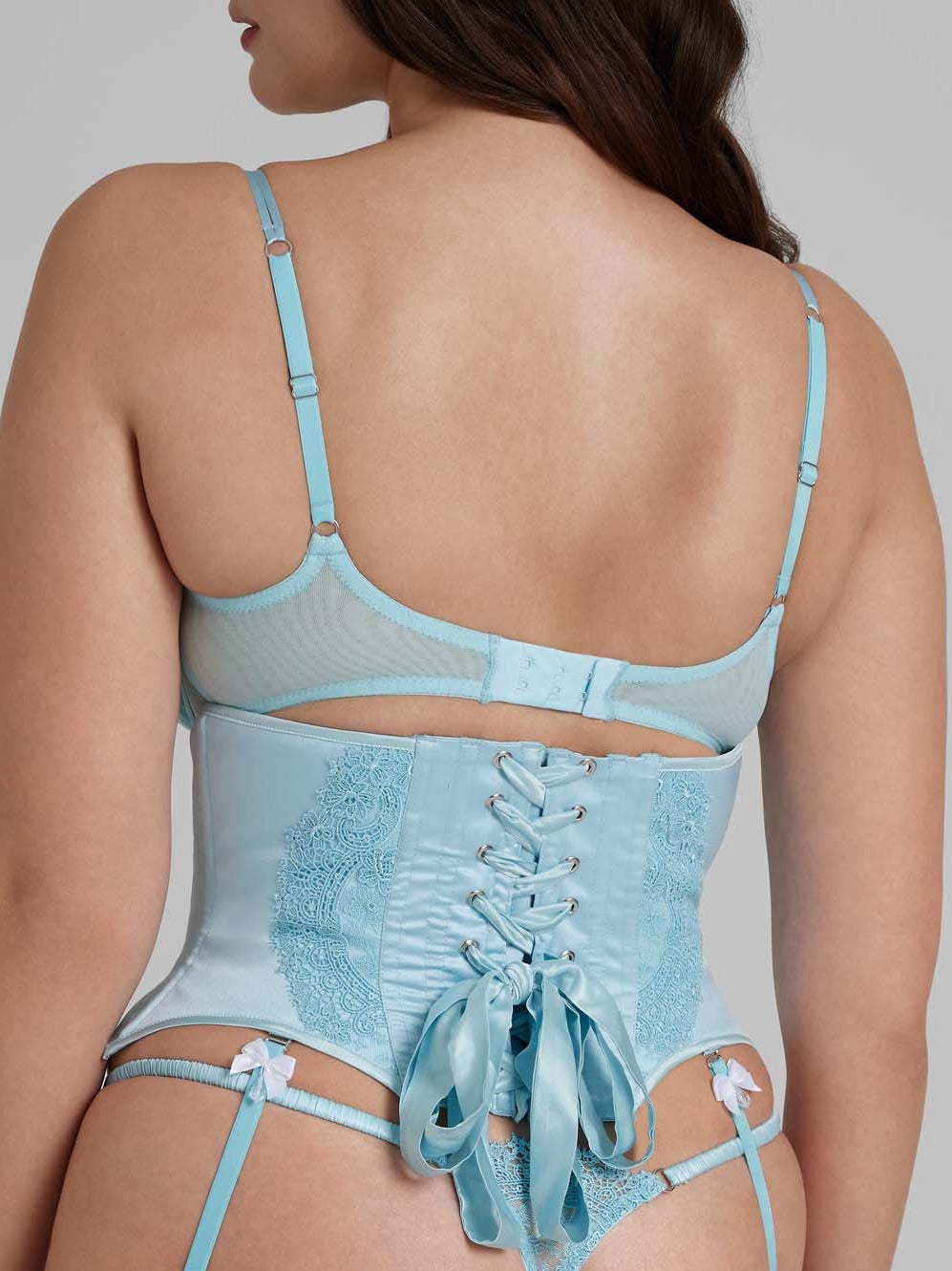 Women wearing blue lace bra and thong with white bows, and waspie with suspender straps from behind