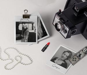 Polaroid camera on a desk with pictures of women, a string of pearls, and lipstick