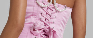 Close up of a woman's back, wearing a pink lace up corset with pearl detailing