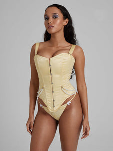 Woman wearing yellow corset with pearl detailing and busk closures and yellow thong with white bows
